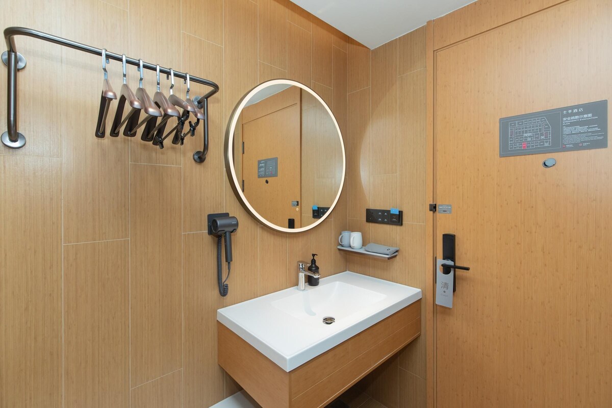 A modern bathroom with a wooden vanity, a sink, a mirror, a towel rack, and a shower area.