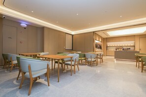 A modern dining area with wooden tables and chairs, a kitchen in the background, and a ceiling with recessed lighting. - Ji Guangzhou Beijing Road Tuanyida Square (Guangzhou)