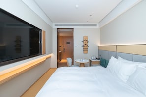 Une chambre d’hôtel avec un grand lit, une table de chevet, une petite table ronde, une chaise, un téléviseur et une armoire contenant des vêtements suspendus.