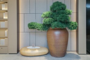 Un interior moderno con una planta grande en maceta, un taburete de madera y una estantería frente a una pared de azulejos.