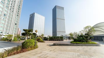 A modern urban plaza with two tall buildings, landscaped areas, and a curved structure.