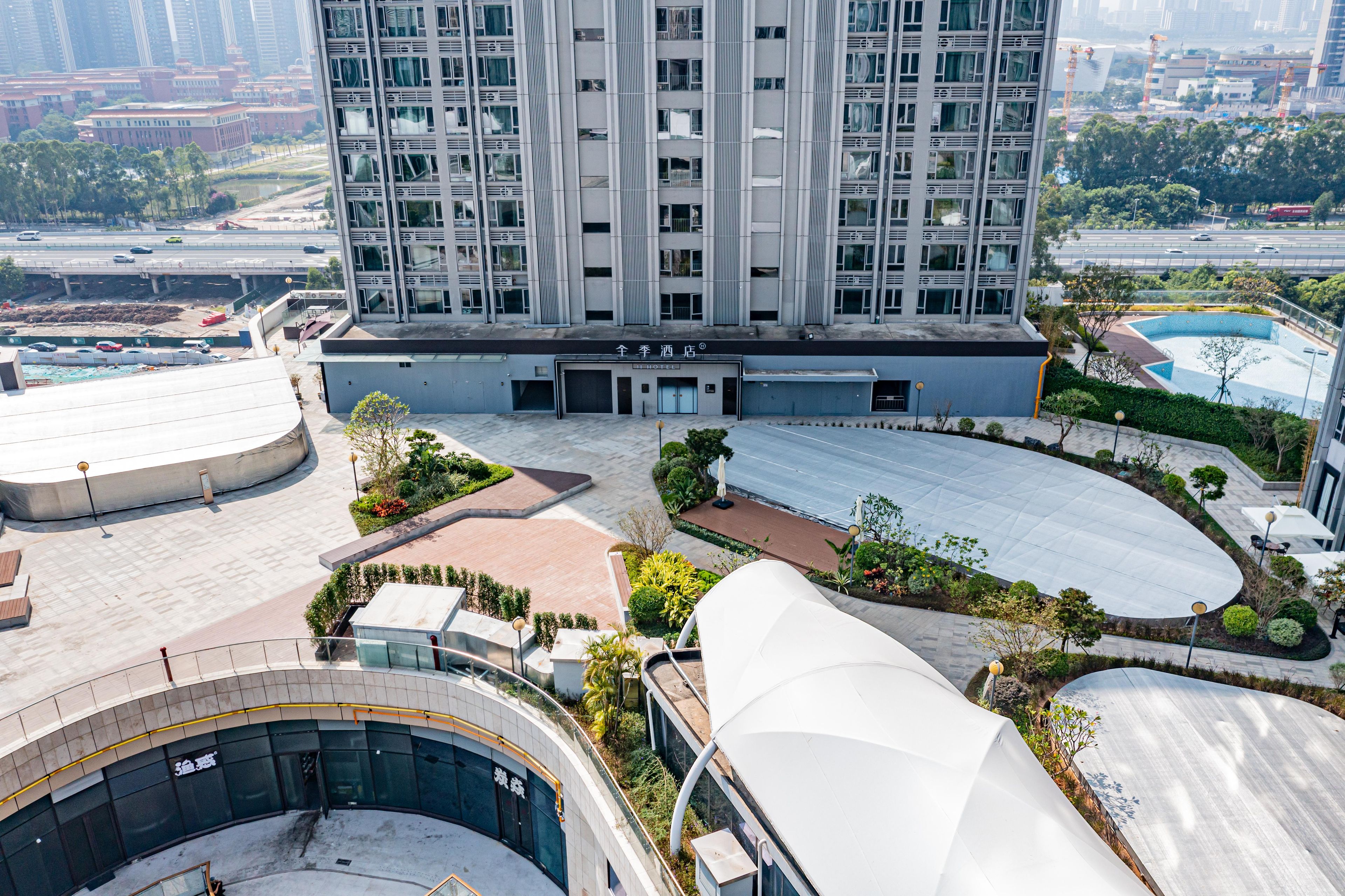 Un hôtel de grande hauteur au design moderne, doté d’une cour intérieure avec une piscine, entourée d’espaces paysagers et d’une promenade couverte.