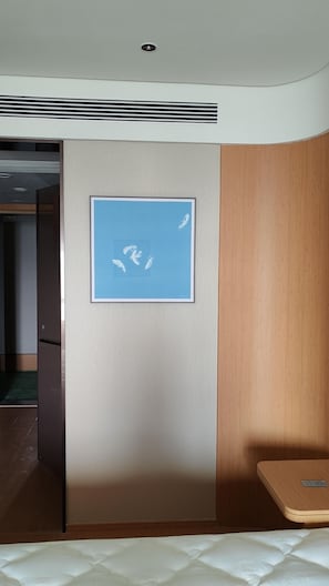 A hotel room with a bed, a wooden panel wall, a framed artwork of feathers, and a small table.