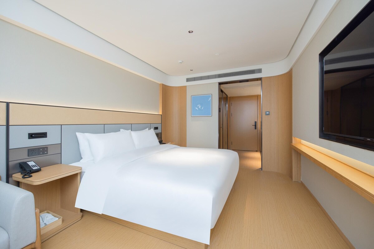 Una habitación de hotel moderna con una cama grande, una mesita de noche con teléfono, un escritorio pequeño y una ventana.