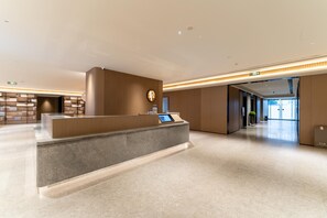 Una moderna zona de recepción con mostrador de mármol, una pantalla digital y un panel de pared de madera.