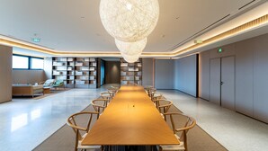A conference room with a long wooden table, chairs, a large hanging light fixture, bookshelves, and a sofa. - Ji Guangzhou Nansha Phoenix Avenue Huanyu City (Guangzhou)