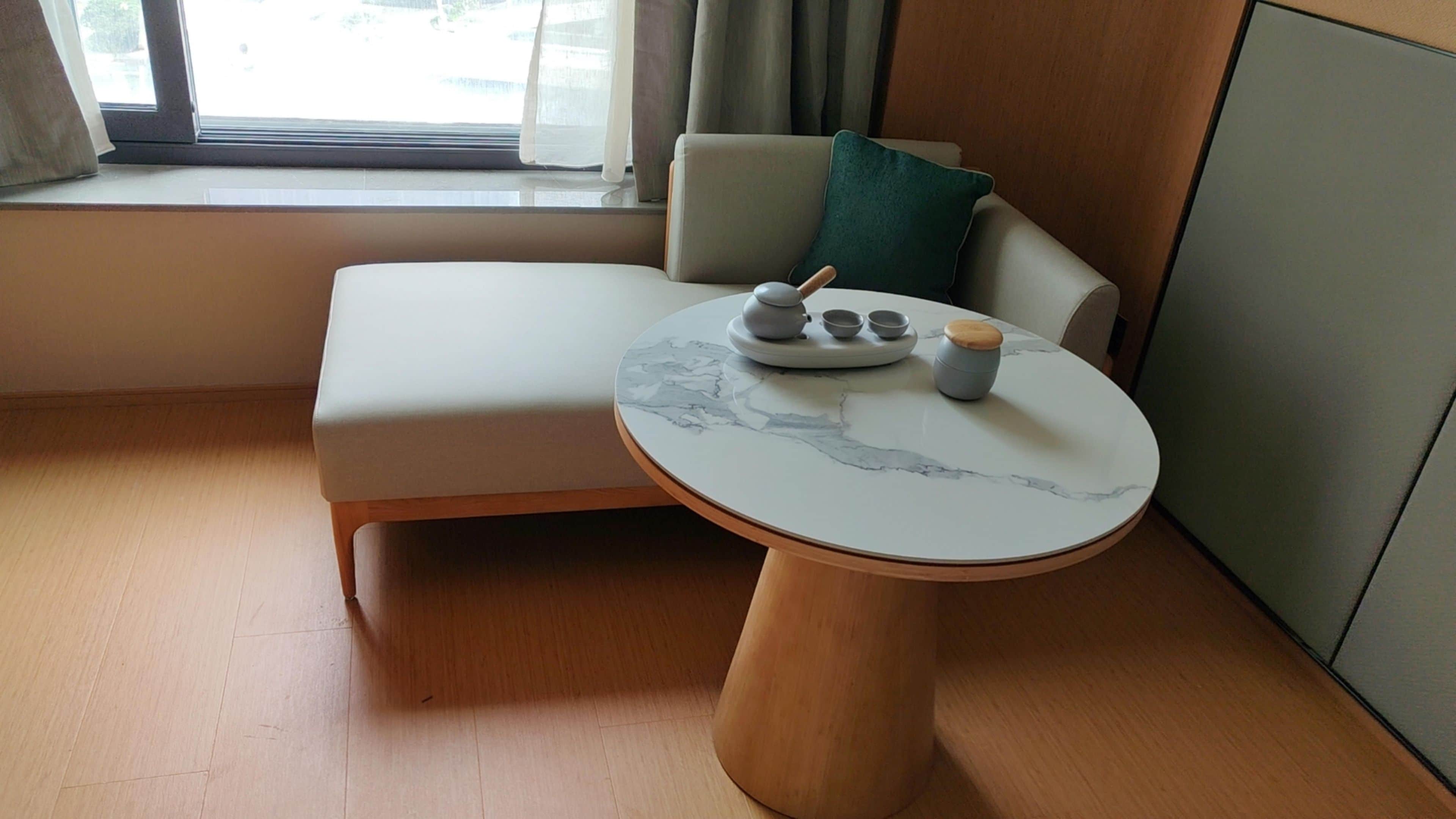 A modern room with a sofa, a round table with a marble top, and a window with curtains.