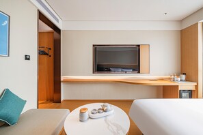 Una habitación de hotel moderna con una cama, una pequeña mesa redonda con una bandeja de té y tazas, un televisor montado en una pared de madera y una zona de kitchenette.