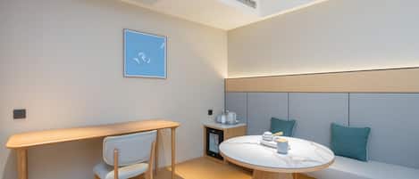 A modern room with a wooden desk, a round table, a sofa, and a wall-mounted shelf.