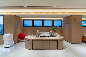Una zona de recepción moderna con un mostrador central, una silla roja y un amplio ventanal con vista a la ciudad.