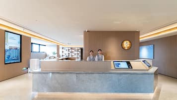 A modern reception desk with two staff members, a digital screen, and a wooden accent wall.