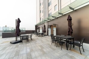 Un patio al aire libre con mesas, sillas y sombrillas, y una fachada moderna de edificio.