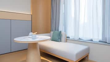 A modern room with a minimalist design, featuring a wooden bench, a round table with a white surface, and a window with sheer curtains.