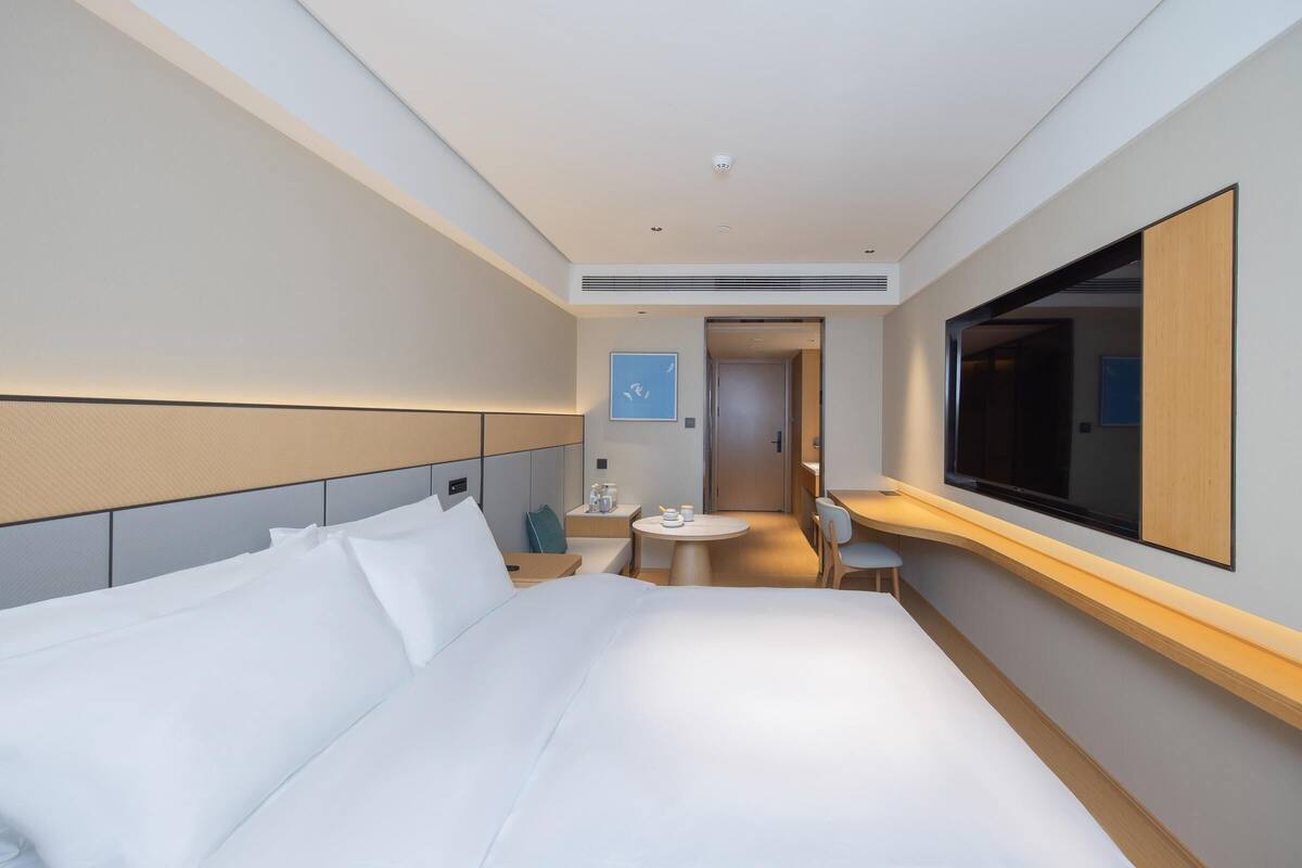 Una camera d'albergo moderna con un letto grande, un comodino, un tavolino piccolo con sedie e un grande specchio a parete.