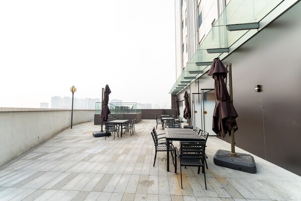 Una terraza en la azotea con mobiliario exterior, barandilla de cristal y vistas a la ciudad.