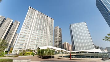 A modern high-rise building with a prominent sign, surrounded by other tall buildings and a landscaped area with plants.