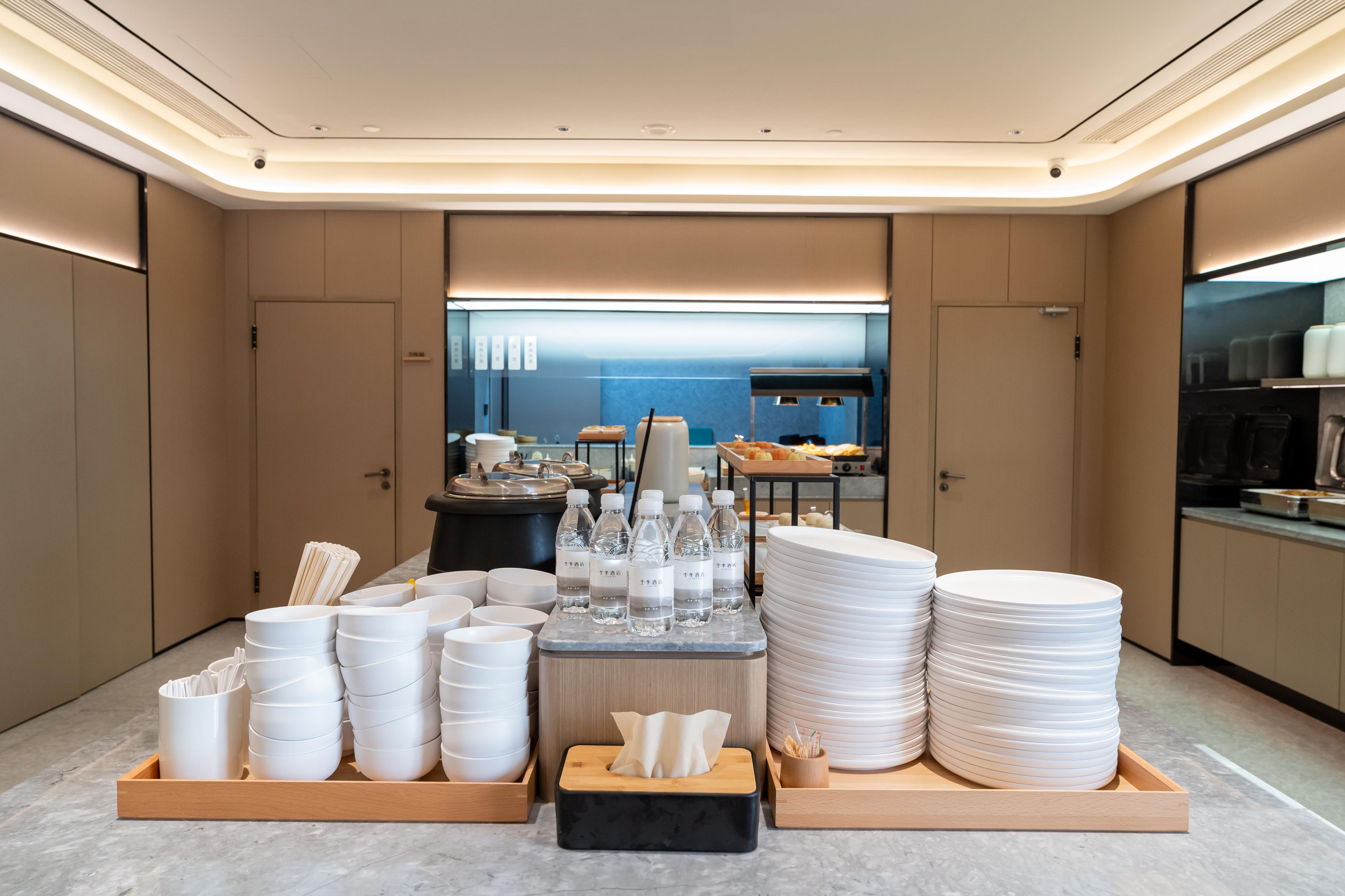 A modern hotel lobby with a reception desk, a view of the sea, and neatly arranged white plates and bowls on wooden trays.