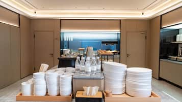 A modern hotel lobby with a reception desk, a view of the sea, and neatly arranged white plates and bowls on wooden trays.