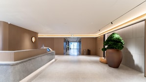 A modern hotel lobby with a reception desk, a large potted plant, and a clear view of the hallway leading to the exit. - Ji Guangzhou Nansha Phoenix Avenue Huanyu City (Guangzhou)