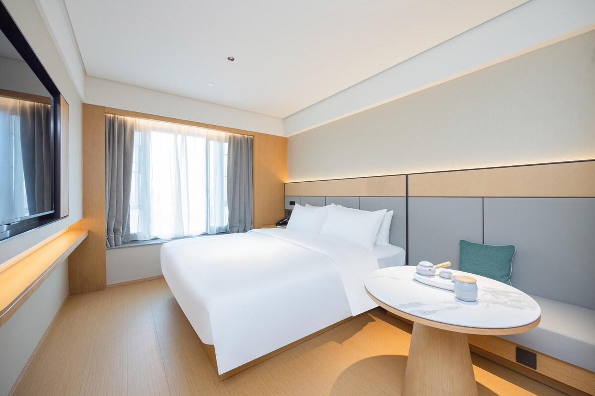 Una habitación de hotel moderna con una cama grande, una mesita de noche y vistas a la ciudad.