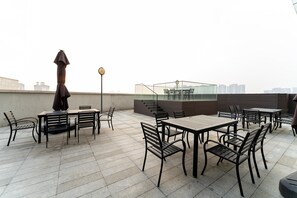 Una terraza en la azotea con mobiliario exterior, barandilla de cristal y vistas al horizonte de la ciudad.