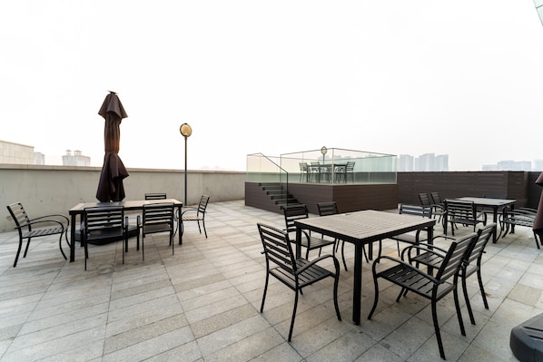 Una terraza en la azotea con mobiliario exterior, barandilla de cristal y vistas al horizonte de la ciudad.