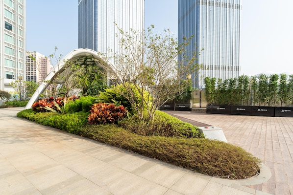 A landscaped area with a curved white structure, surrounded by various plants and shrubs.