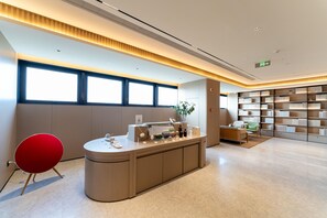 Un área de recepción moderna con mostrador, una silla roja, una estantería y un ventanal grande.