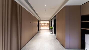 A modern hotel corridor with a straight path, recessed lighting, and a central plant.