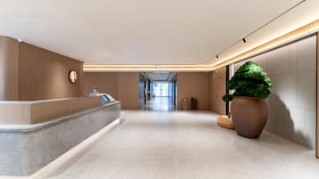 A modern hotel lobby with a reception desk, a large potted plant, and a clear view of the hallway leading to the exit.