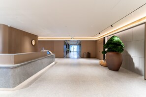 A modern hotel lobby with a reception desk, a large potted plant, and a clear view of the hallway leading to the exit.
