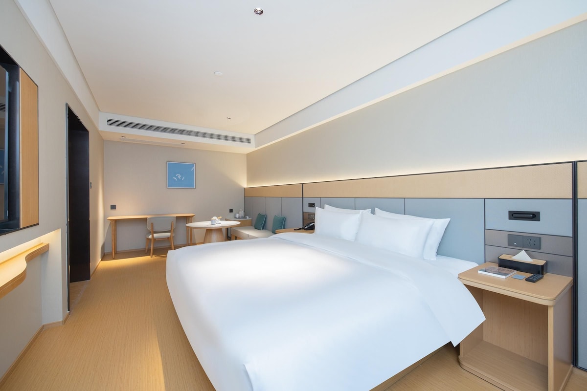 Una habitación de hotel moderna con una cama grande, una mesita de noche y un escritorio con una silla.