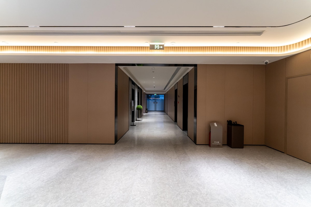 A modern hotel hallway with a long corridor, a trash bin, and a potted plant.