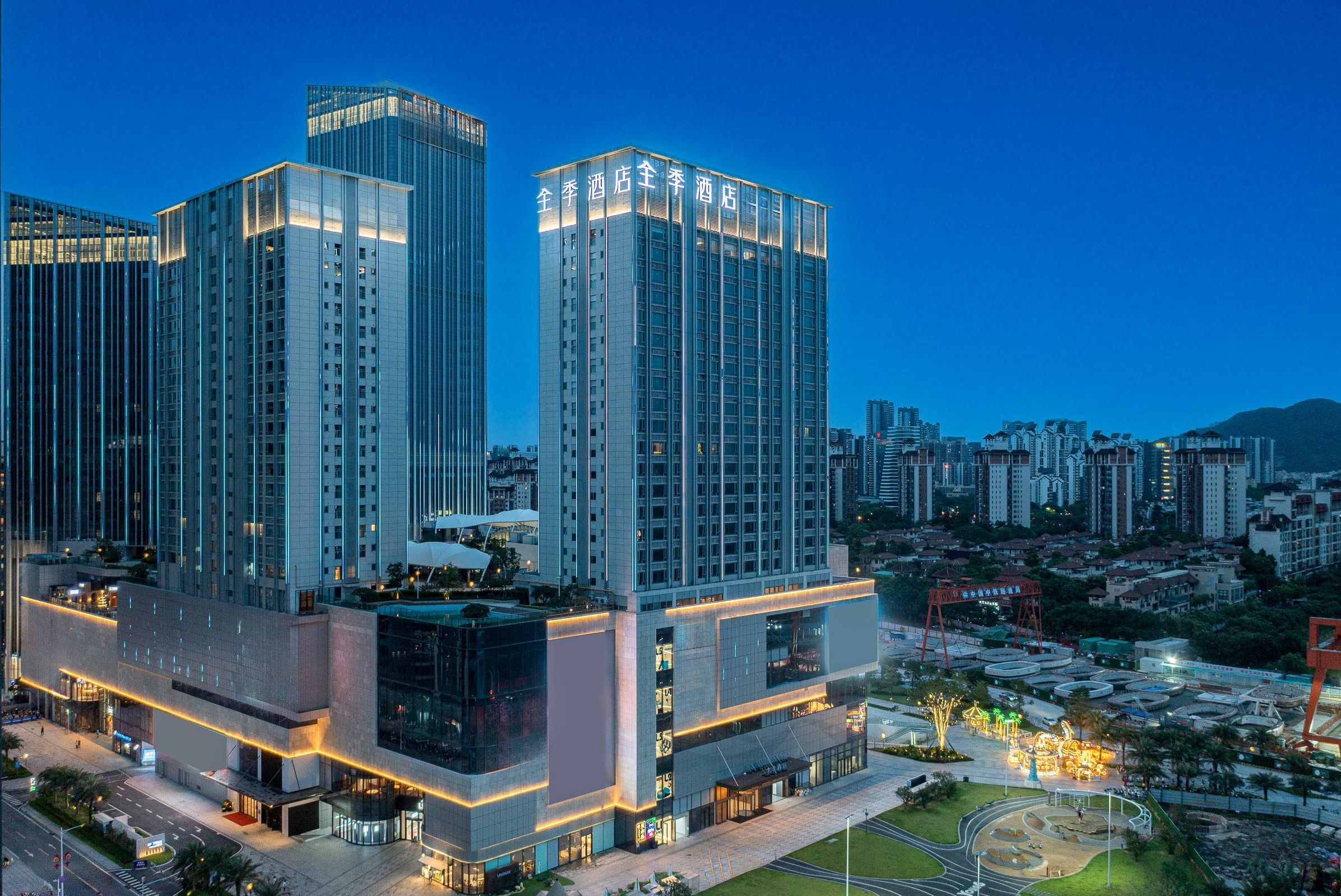 A modern hotel with multiple high-rise buildings, featuring a prominent glass facade and illuminated signage.