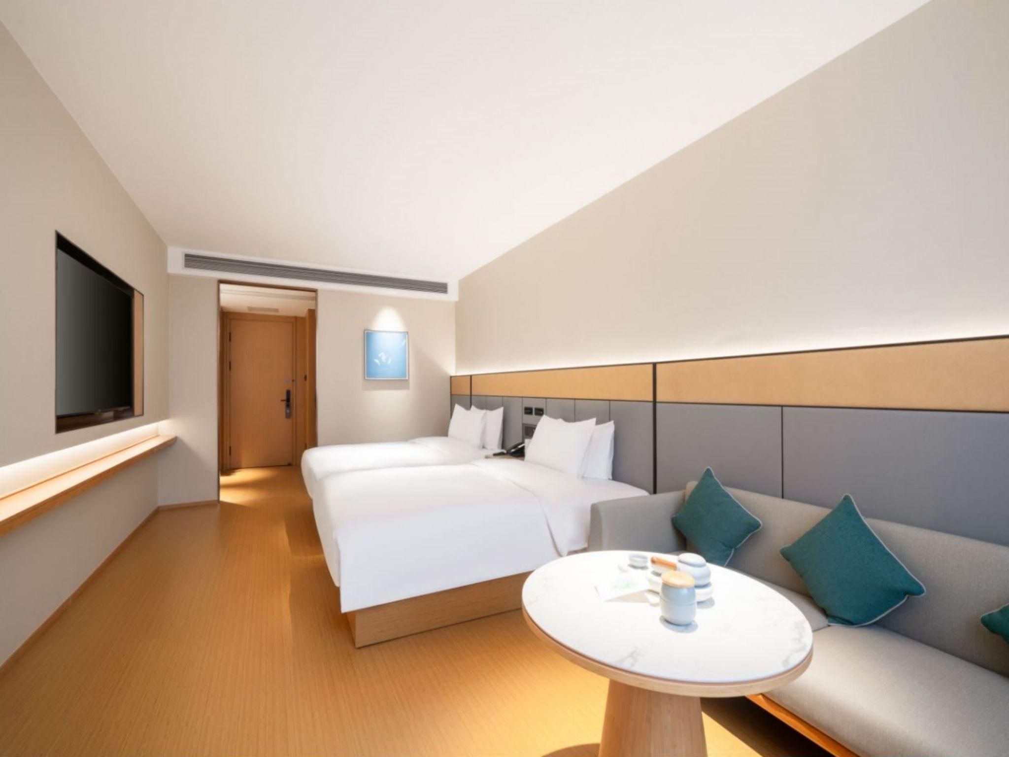 A modern hotel room with a large bed, a sofa, a round table, and a TV mounted on the wall.