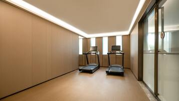 A modern, well-lit room with two treadmills, a large window, and a glass partition.