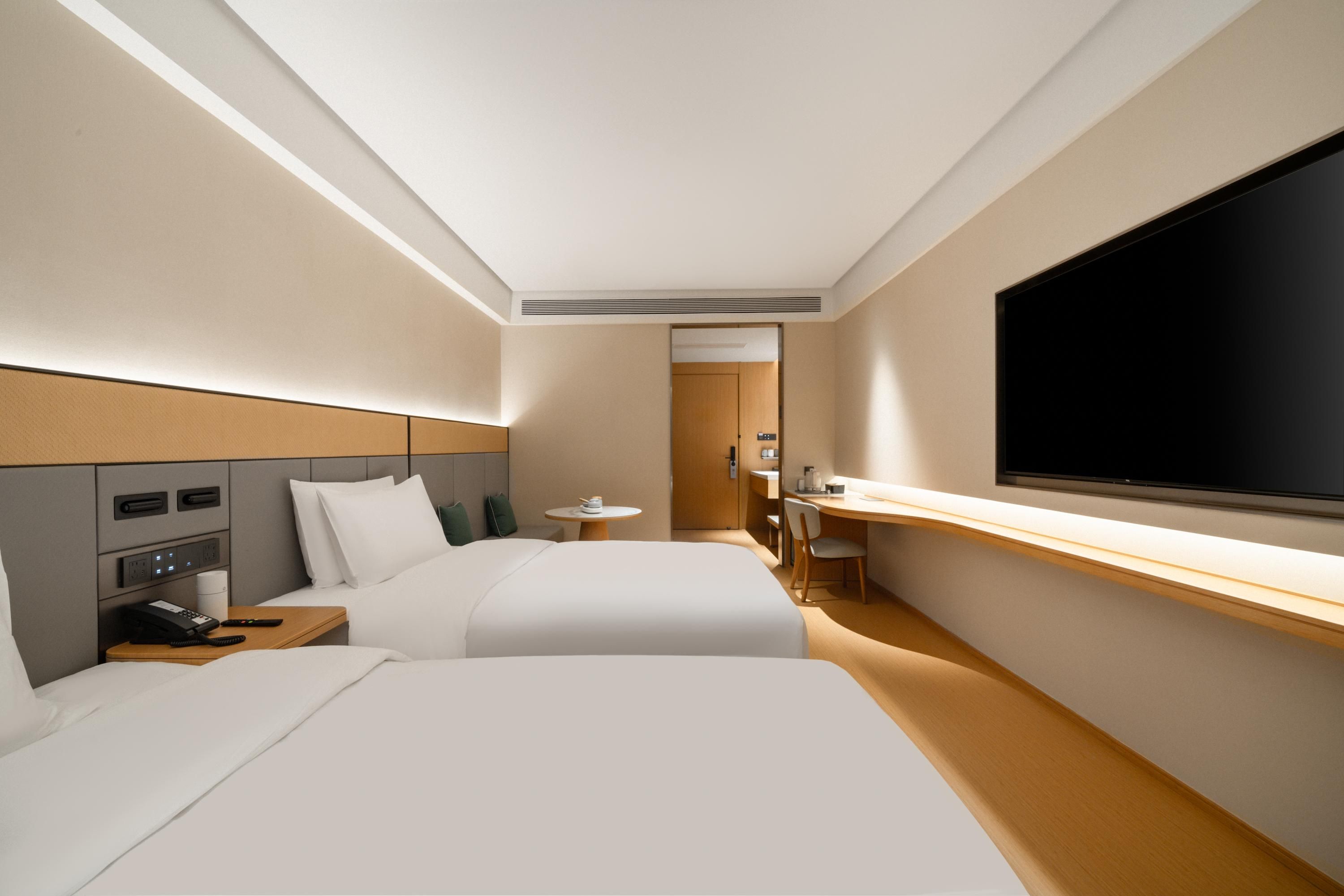 A modern hotel room with two beds, a desk, a flat-screen TV, and a small table.