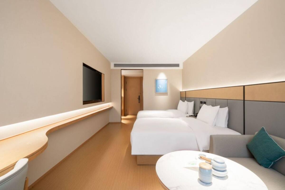 A hotel room with two beds, a TV, a bedside table, and a small seating area.