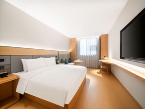 Een moderne hotelkamer met een groot bed, een bureau, een televisie en een raam met gordijnen.