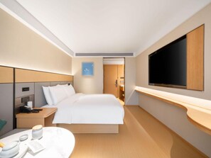 Een moderne hotelkamer met een groot bed, een nachtkastje met telefoon en lamp, een flatscreen televisie aan de wand en een klein rond tafeltje met kop en schotel.