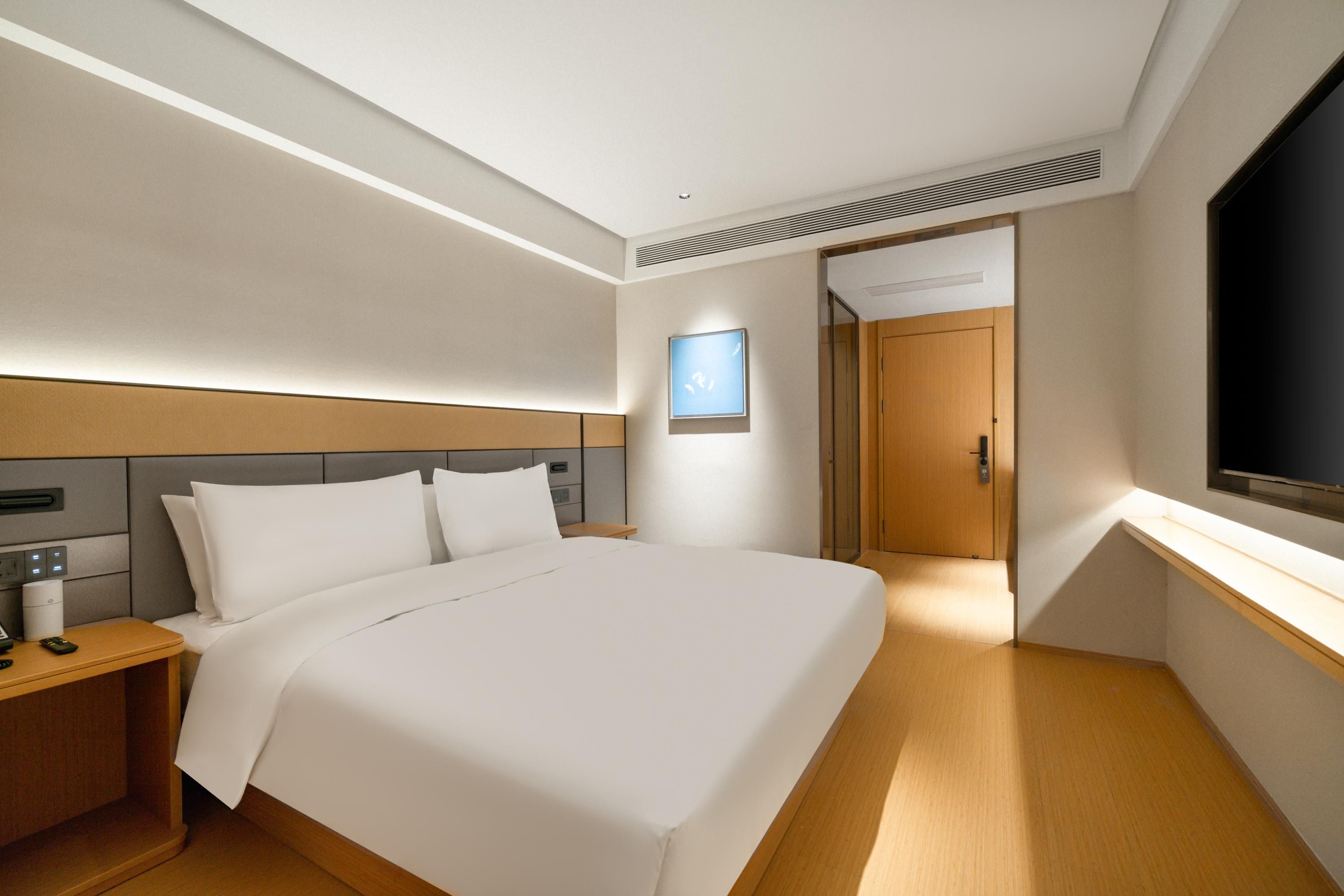 Ein modernes Hotelzimmer mit einem großen Bett, Nachttischen, einem Flachbildfernseher und einer Tür zu einem weiteren Raum.