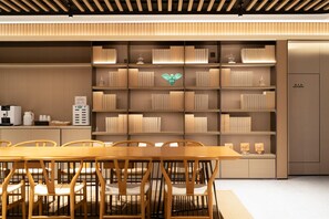 A modern dining area with a wooden table and chairs, a bookshelf with decorative items, and a kitchen area with appliances. - Ji Guangzhou Liwan TCL Yunfeng Technology Park (Guangzhou)