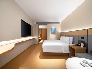 Une chambre d’hôtel moderne avec un grand lit, des tables de chevet, une télévision et un petit bureau équipé d’un téléphone et d’une tasse.