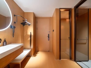 A modern bathroom with a wooden vanity, a round mirror, a handheld showerhead, and a glass shower enclosure.