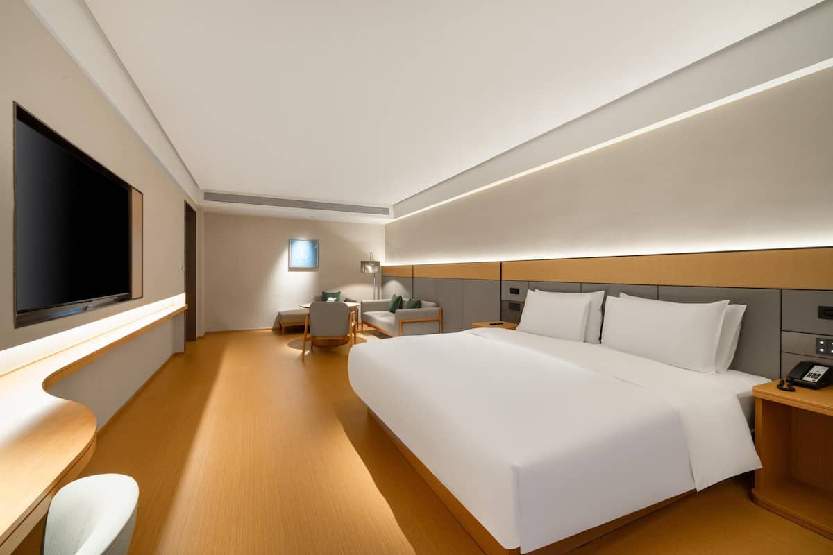 A modern hotel room with a large bed, a desk, a flat-screen TV, and a bedside table with a phone.