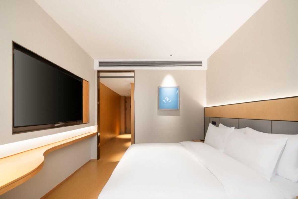 Een moderne hotelkamer met een groot bed, een flatscreen televisie aan de muur, een houten nachtkastje en een ingelijst kunstwerk.