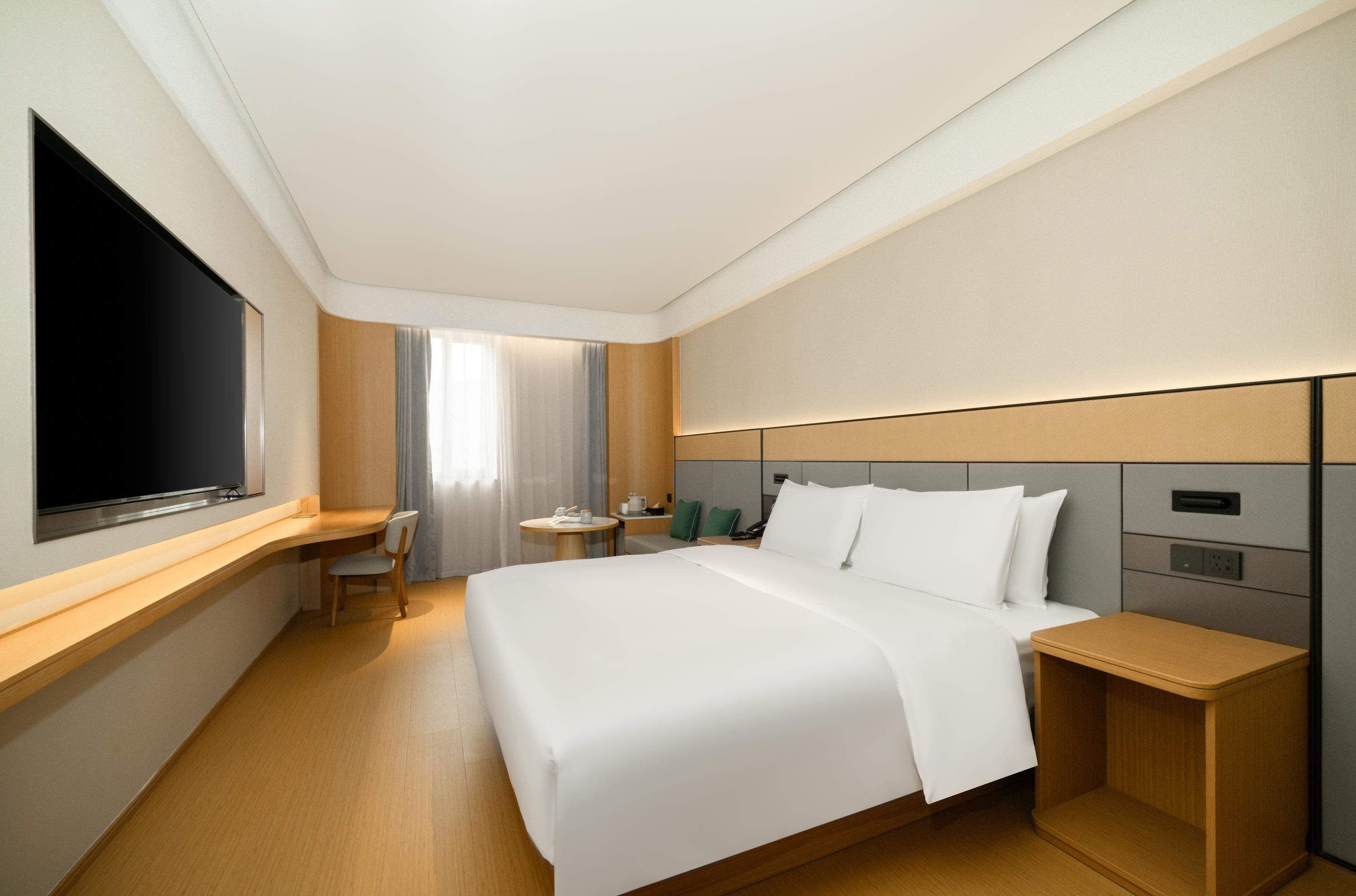 A hotel room with a large bed, a desk, a TV, and a bedside table.