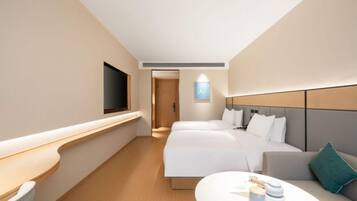 Habitación de hotel con dos camas, televisor, mesita de noche y un pequeño espacio para sentarse.