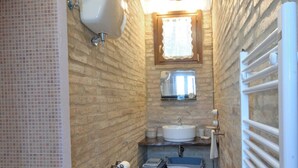 A narrow bathroom with a tiled floor, a white toilet, a bidet, a sink, and a shower area. - DEPENDANCE ON THE GARDEN (Uncinano, Spoleto)