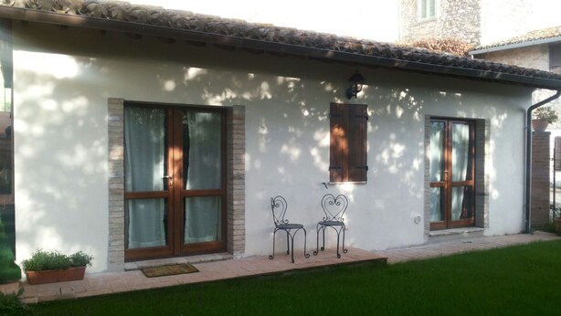 A white building with two large windows and a door, a small patio with two metal chairs, and a potted plant. - DEPENDANCE ON THE GARDEN (Uncinano, Spoleto)
